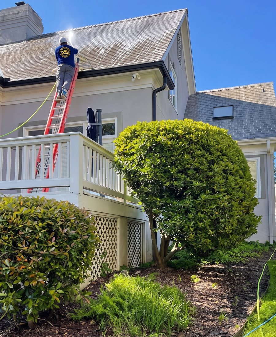 Sean on a ladder soft washing a roof in a Concord Home Exteriors shirt